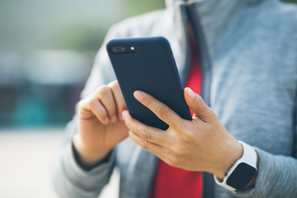 Woman using smartphone outdoors, casual attire.